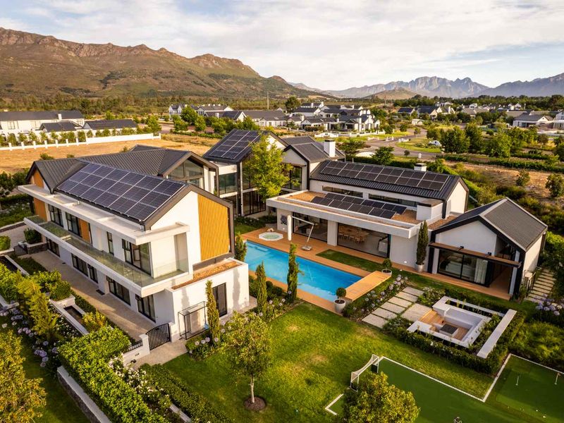 Stunning aerial view of a modern luxury residence featuring extensive solar panel arrays, a private swimming pool, and beautifully landscaped gardens in a scenic estate.