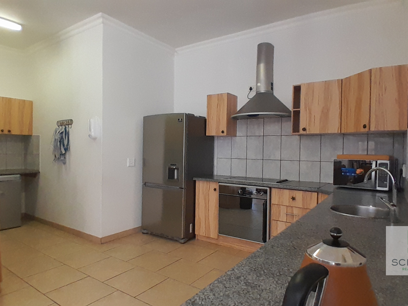 A functional kitchen featuring wooden cabinetry, granite-look countertops, a built-in oven with extractor fan, and tiled flooring throughout.