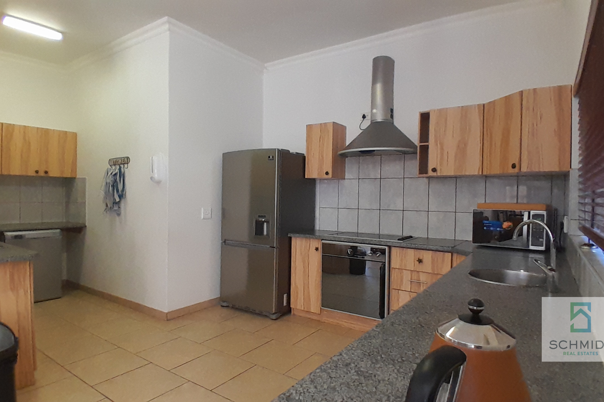 A functional kitchen featuring wooden cabinetry, granite-look countertops, a built-in oven with extractor fan, and tiled flooring throughout.