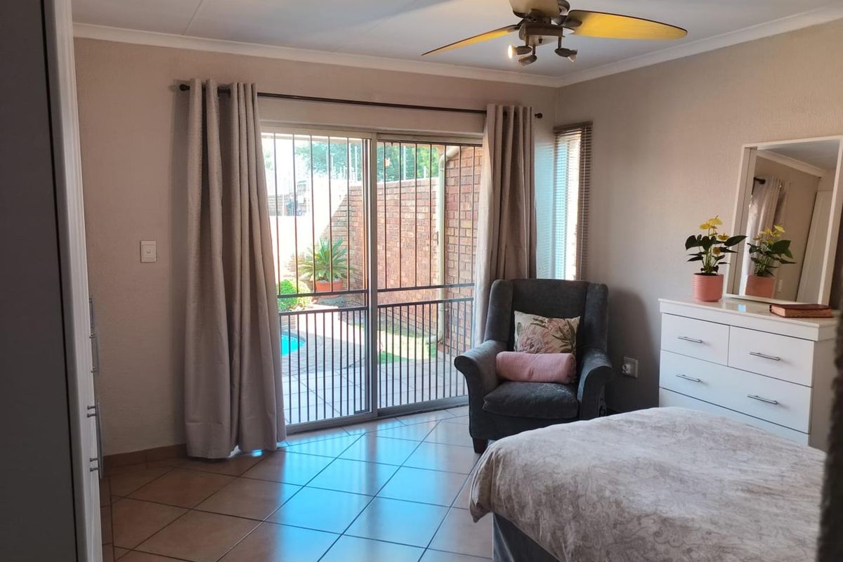 A well-lit bedroom featuring tiled flooring, a ceiling fan, and a sliding glass door providing direct access to the outdoor pool area.