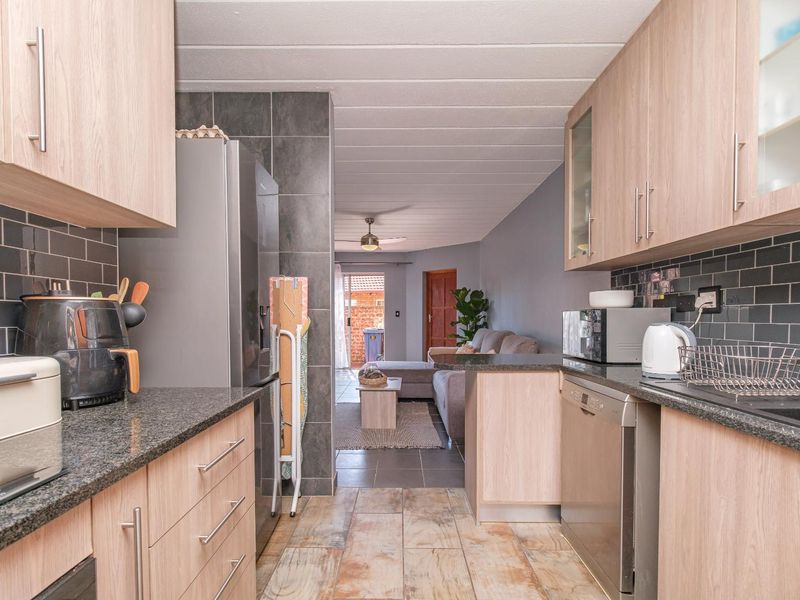Open-plan kitchen featuring light wood cabinetry, granite countertops, and subway tile backsplash, flowing seamlessly into the adjacent living area.