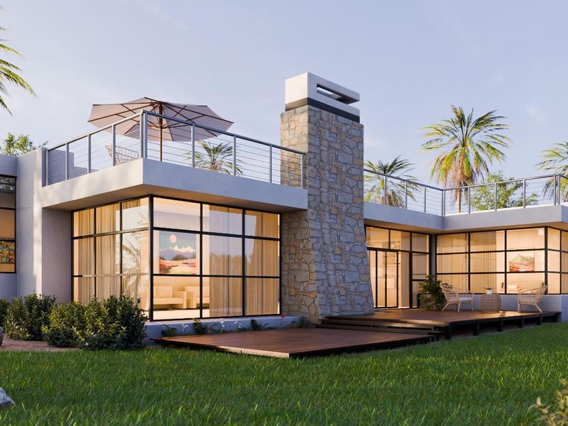 A modern architectural rear elevation featuring large steel-framed windows, a prominent stone chimney, and an expansive timber deck overlooking the garden.
