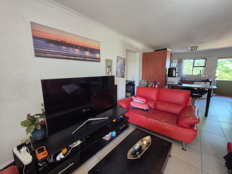Open-plan living area featuring tiled flooring and a connected kitchen space with a breakfast bar, offering a functional layout for modern living.