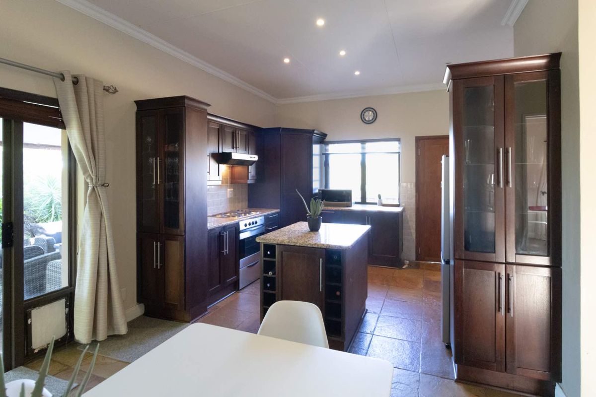 A well-appointed kitchen featuring dark wood cabinetry, granite countertops, a central island with built-in wine storage, and tiled flooring.