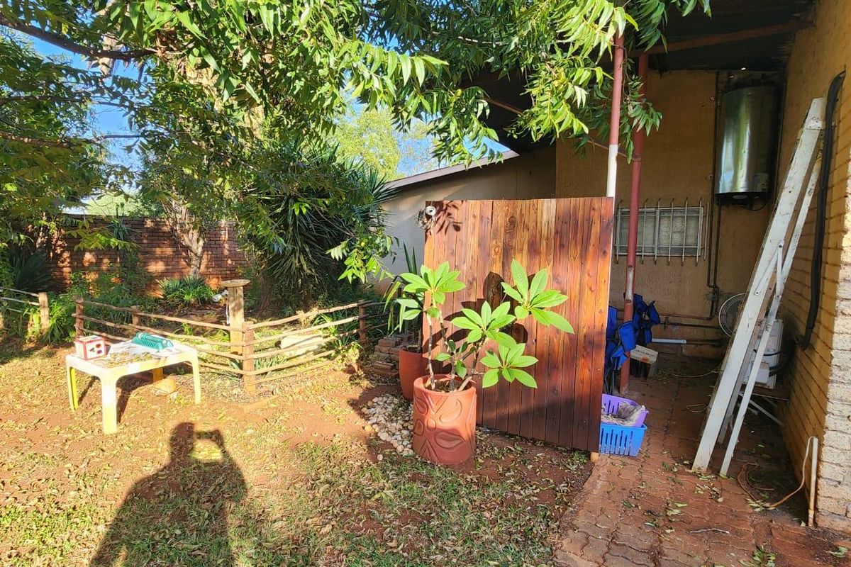 A rear garden area featuring a wooden privacy screen, paved walkway, and exterior wall-mounted geyser unit.