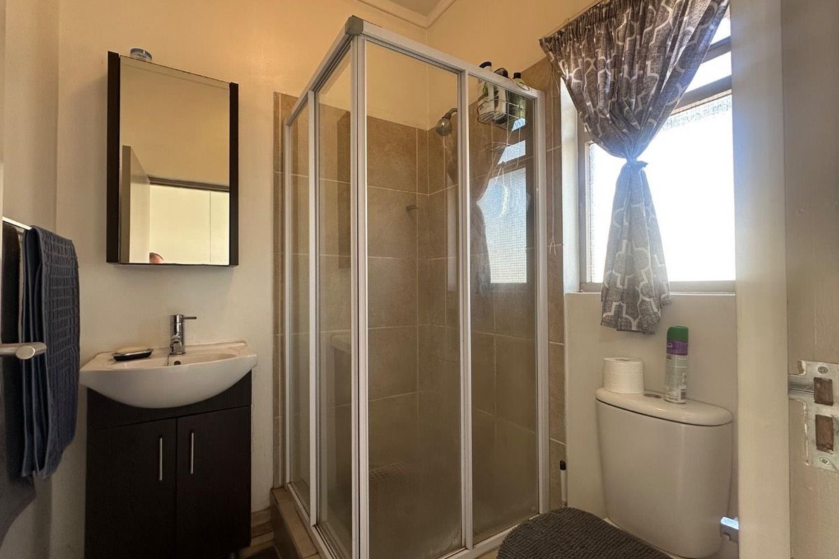 A functional bathroom featuring a corner shower enclosure, a vanity unit with a basin, and a standard toilet.