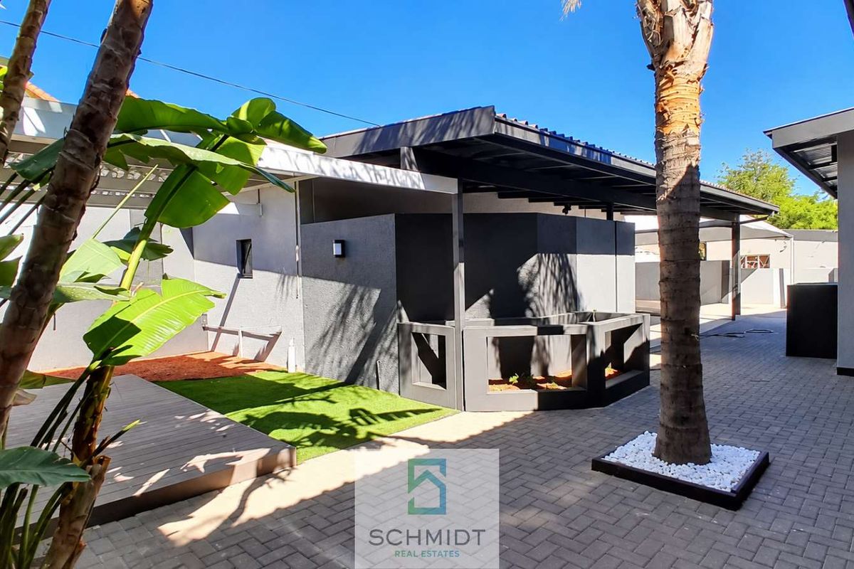 A well-maintained rear exterior area featuring a paved courtyard, covered patio space, timber decking, and artificial lawn with modern architectural finishes.