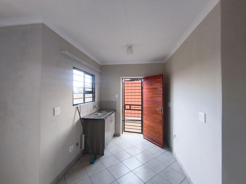 A clean, empty scullery or utility area featuring a built-in sink unit, tiled flooring, and direct access to the exterior via a security gate.