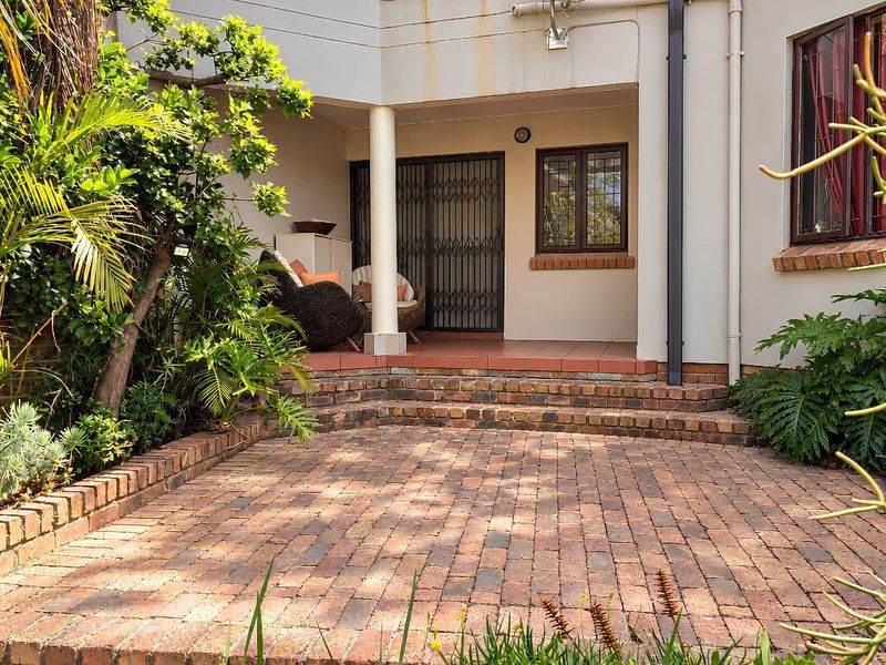 A paved outdoor patio area featuring brick steps, established garden surroundings, and a covered entrance with a security gate.