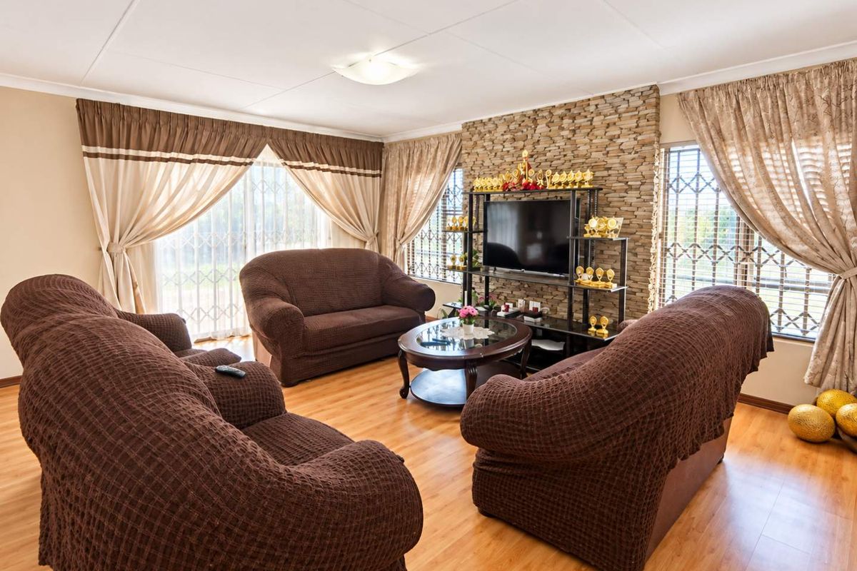 A comfortable living room featuring a stone-clad feature wall, laminate flooring, and large windows fitted with security gates.