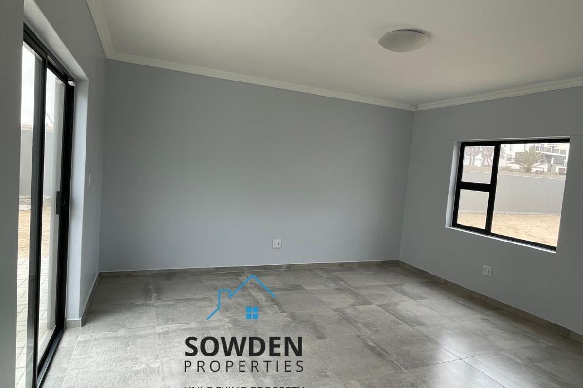 A bright, empty living room featuring large windows, sliding glass doors, and modern tiled flooring, offering a clean and neutral space.