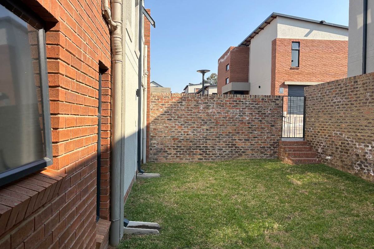 A private rear garden area featuring a brick boundary wall, lawn, and a small set of steps leading to a gated side access.