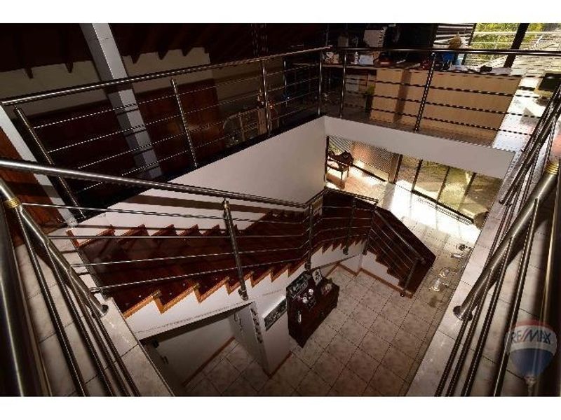 A high-angle view of an open-plan interior featuring a wooden staircase with stainless steel balustrades and tiled flooring.