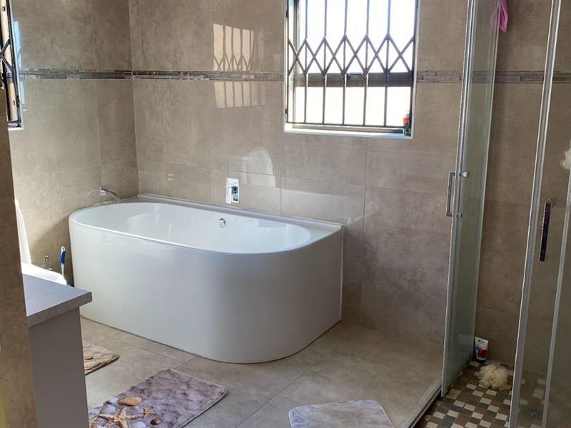 Modern bathroom featuring a freestanding bathtub, separate shower enclosure, and neutral floor-to-ceiling tiling with security bars on the window.
