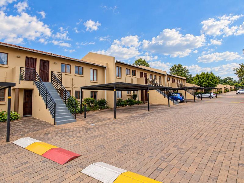 Exterior view of an apartment complex featuring paved parking areas, covered carports, and external staircases leading to upper-level units.