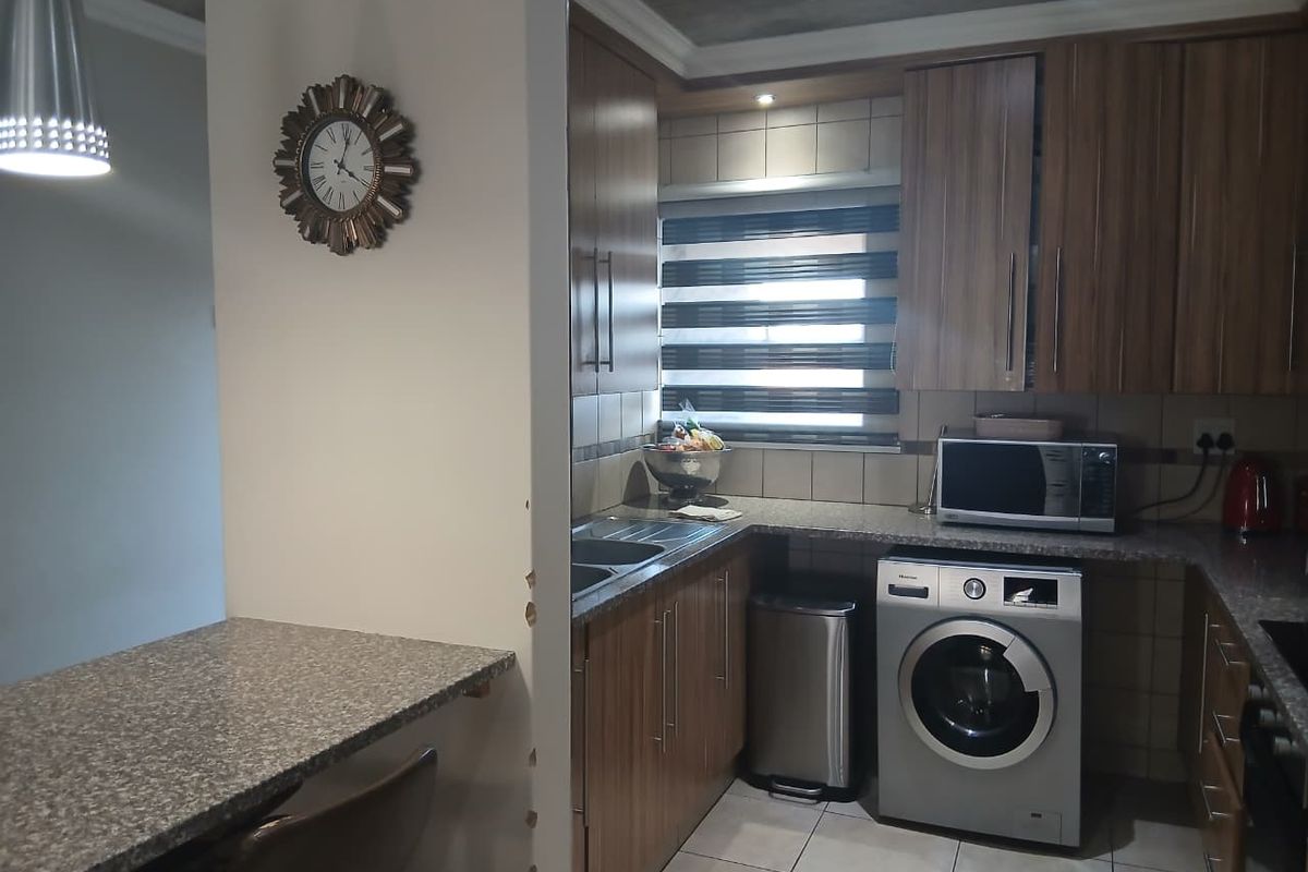 A functional kitchen featuring wood-finish cabinetry, granite countertops, tiled backsplash, and a breakfast bar, with integrated appliances and tiled flooring.