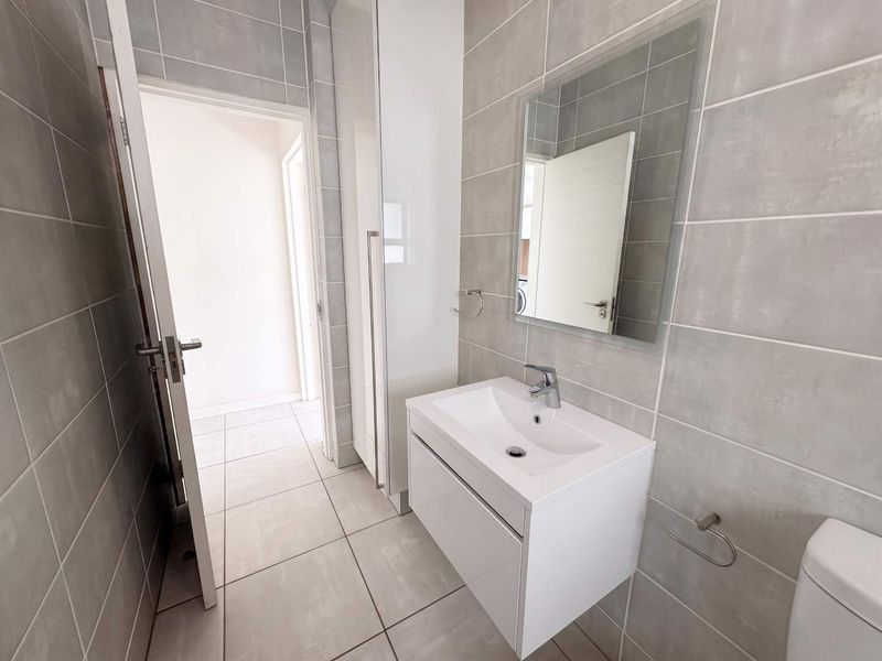 Modern bathroom featuring grey tiled walls and flooring, a sleek wall-mounted vanity with a ceramic basin, and a built-in storage cupboard.