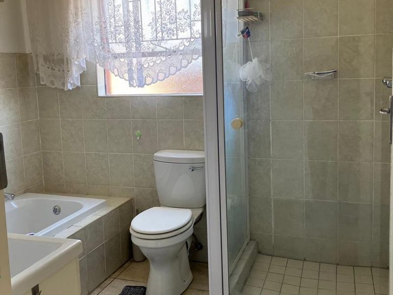 A functional bathroom featuring a built-in bathtub, separate shower enclosure, toilet, and vanity basin with neutral wall and floor tiling.