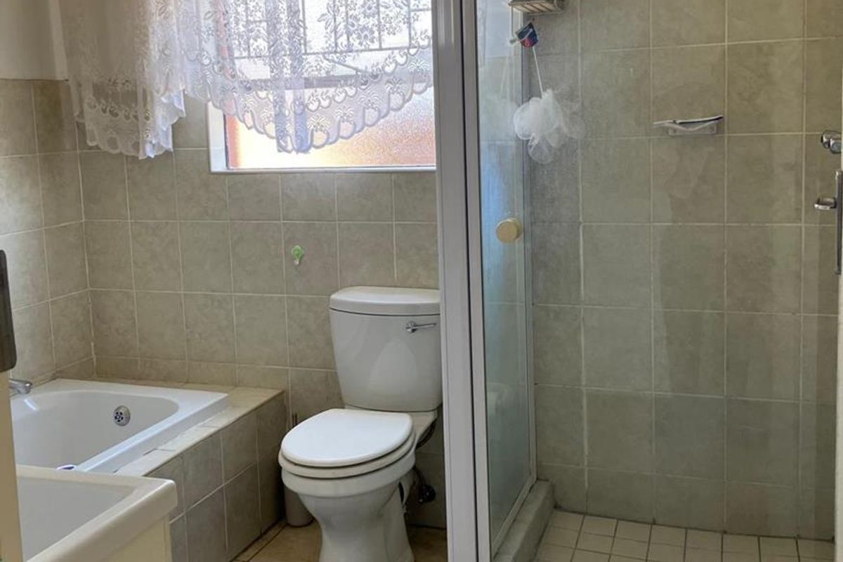 A functional bathroom featuring a built-in bathtub, separate shower enclosure, toilet, and vanity basin with neutral wall and floor tiling.