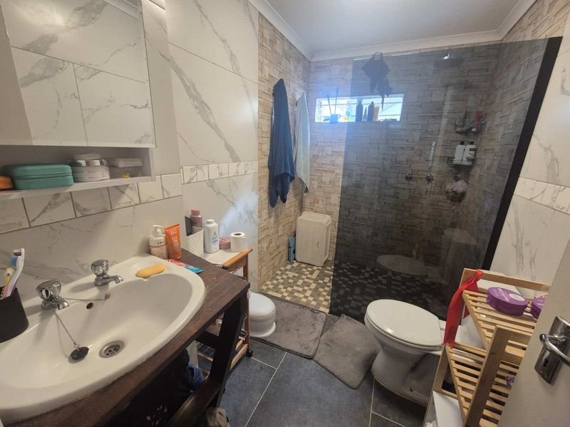 A functional bathroom featuring a walk-in shower with a glass screen, vanity basin, and modern tiled finishes throughout.