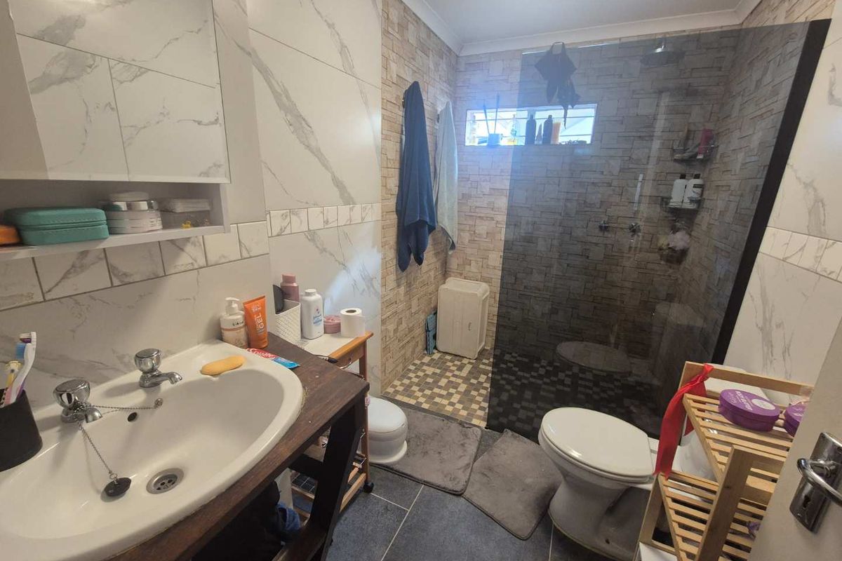 A functional bathroom featuring a walk-in shower with a glass screen, vanity basin, and modern tiled finishes throughout.