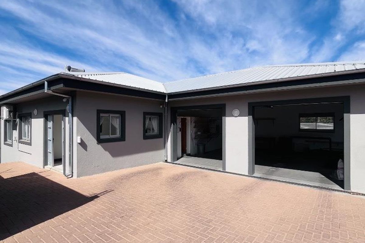 Rear exterior view of the property featuring a paved courtyard area and a double garage with a metal roof.