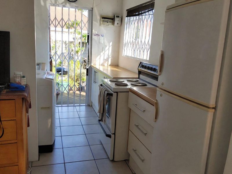 A functional scullery or laundry area featuring tiled floors, built-in cabinetry, a freestanding stove, and direct access to the exterior via a security gate.