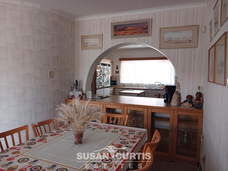Open plan dining area featuring a decorative archway leading into the kitchen with built-in cabinetry and functional counter space.