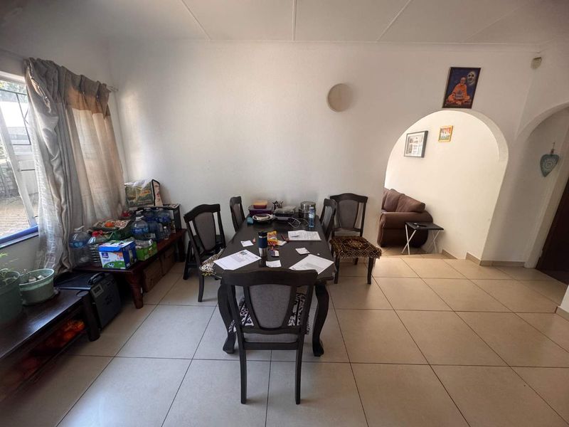 A dining area featuring neutral tiled flooring and a distinctive arched doorway leading to an adjacent living space.