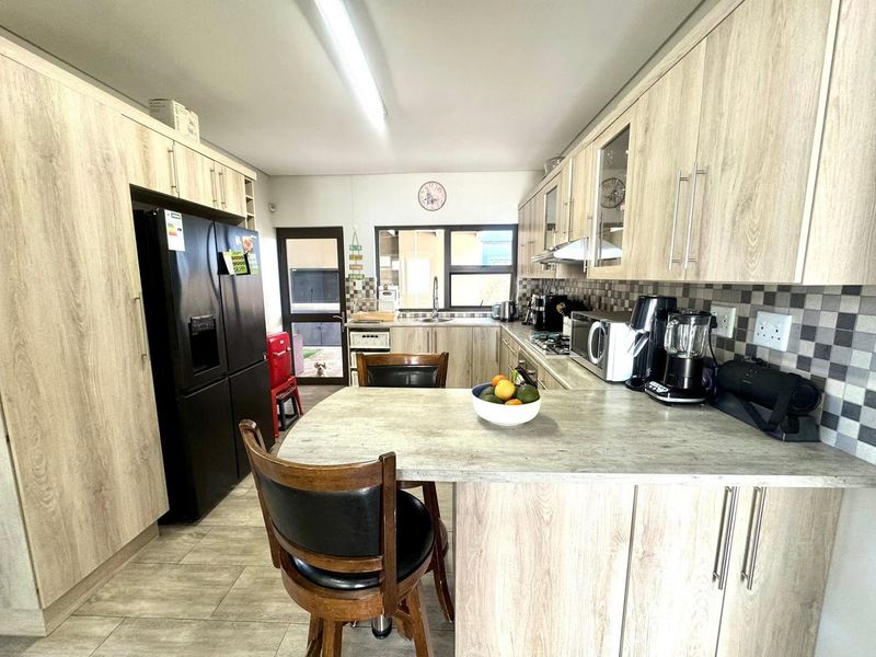 A functional kitchen featuring light wood-grain cabinetry, mosaic tile backsplash, laminate countertops, and tiled flooring with direct access to the exterior.
