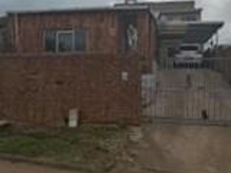 Front exterior view of a townhouse featuring a brick facade, gated driveway, and carport area.