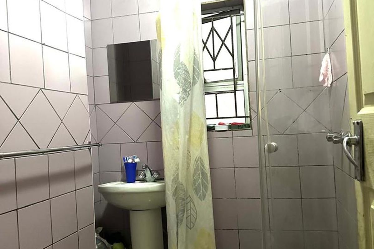 A compact bathroom featuring a pedestal basin, a corner shower enclosure with a glass screen, and full-height wall tiling.