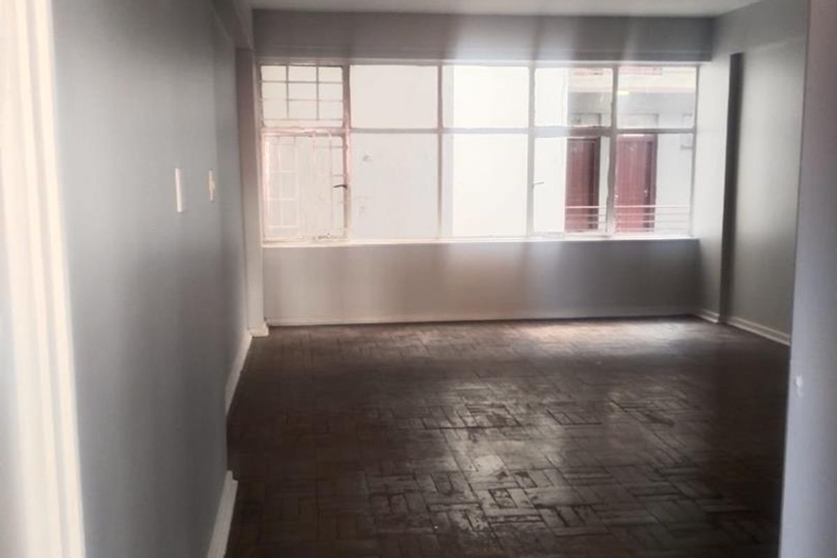 An empty living room featuring original parquet flooring and large windows, providing a blank canvas for renovation and interior design.