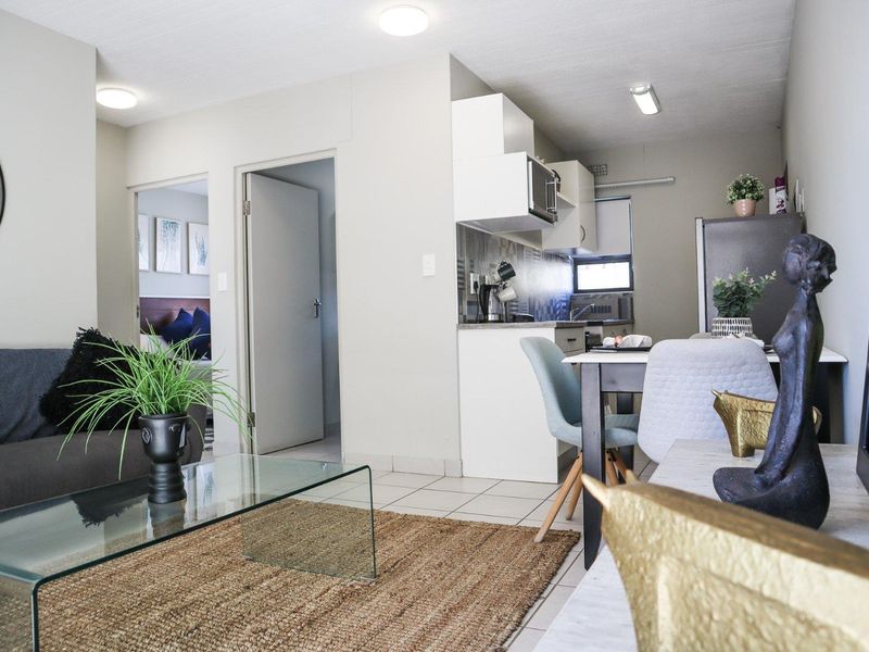 Open plan living area featuring tiled flooring and a compact kitchen with built-in cabinetry and a tiled backsplash.
