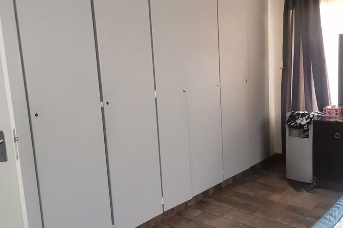 Bedroom featuring a large wall-to-wall built-in wardrobe with grey doors and wood-look tiled flooring.