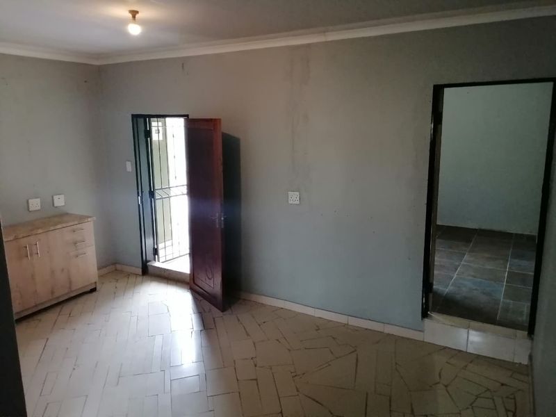An empty living area featuring tiled flooring, coving, and access to an exterior security gate, requiring cosmetic updates to the walls.