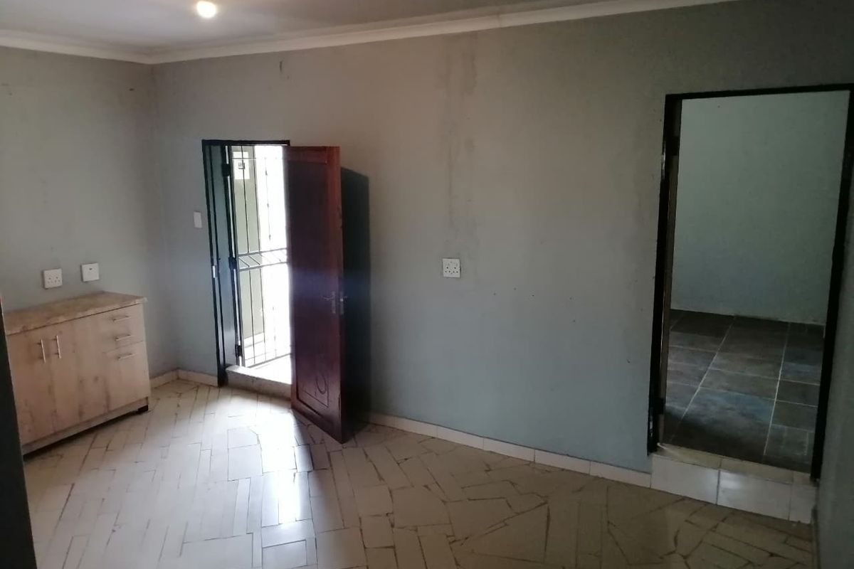 An empty living area featuring tiled flooring, coving, and access to an exterior security gate, requiring cosmetic updates to the walls.