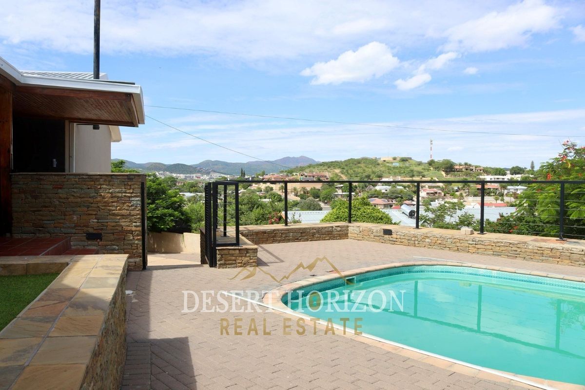 Outdoor pool area featuring stone-clad retaining walls, paved patio space, and metal railings with expansive elevated views of the surrounding landscape.