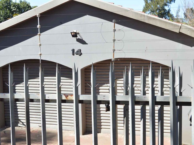 A double garage facade featuring roller shutter doors, secured by perimeter electric fencing and metal security spikes.
