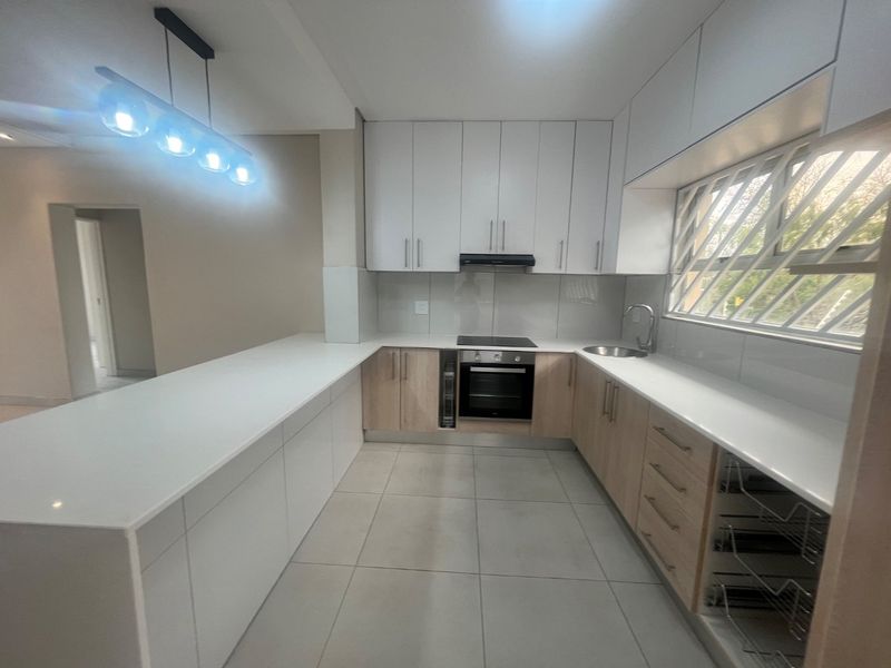 Modern kitchen featuring white and wood-tone cabinetry, quartz countertops, integrated appliances, and tiled flooring in a clean, contemporary layout.