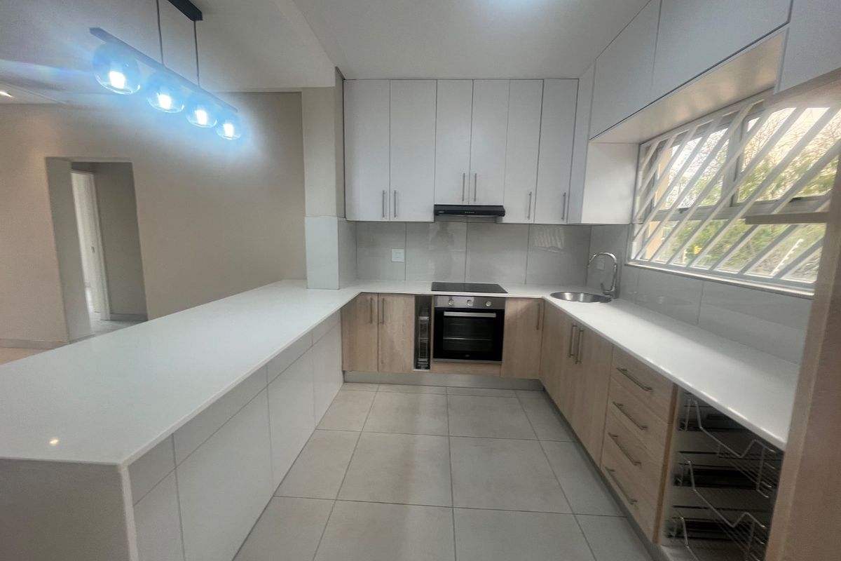 Modern kitchen featuring white and wood-tone cabinetry, quartz countertops, integrated appliances, and tiled flooring in a clean, contemporary layout.