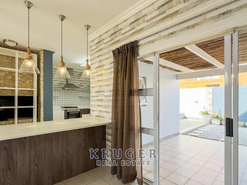 Open-plan kitchen and living area featuring a breakfast bar, stone accent wall, and seamless flow to a covered outdoor patio through sliding glass doors.