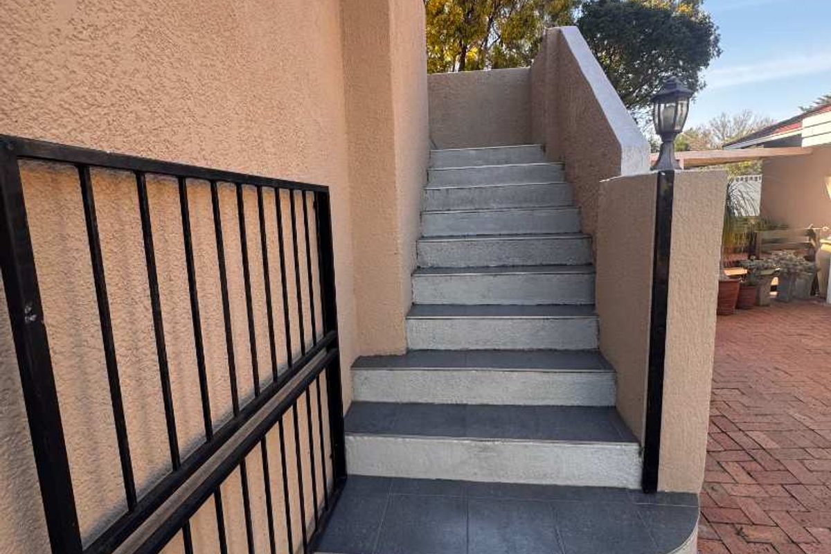 Exterior staircase with tiled steps and metal security gate leading to an upper level, adjacent to a paved patio area.