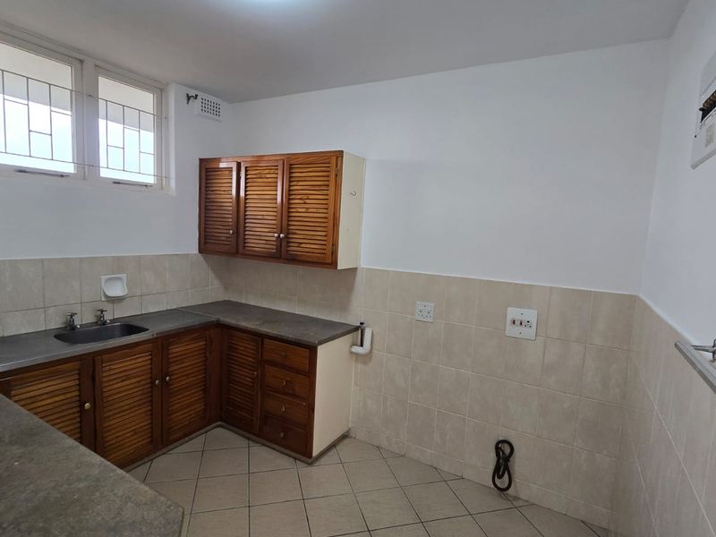 A functional kitchen featuring louvered wooden cabinetry, laminate countertops, a stainless steel sink, and neutral ceramic wall and floor tiling.
