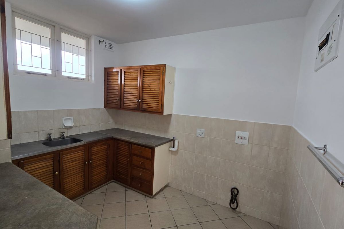 A functional kitchen featuring louvered wooden cabinetry, laminate countertops, a stainless steel sink, and neutral ceramic wall and floor tiling.