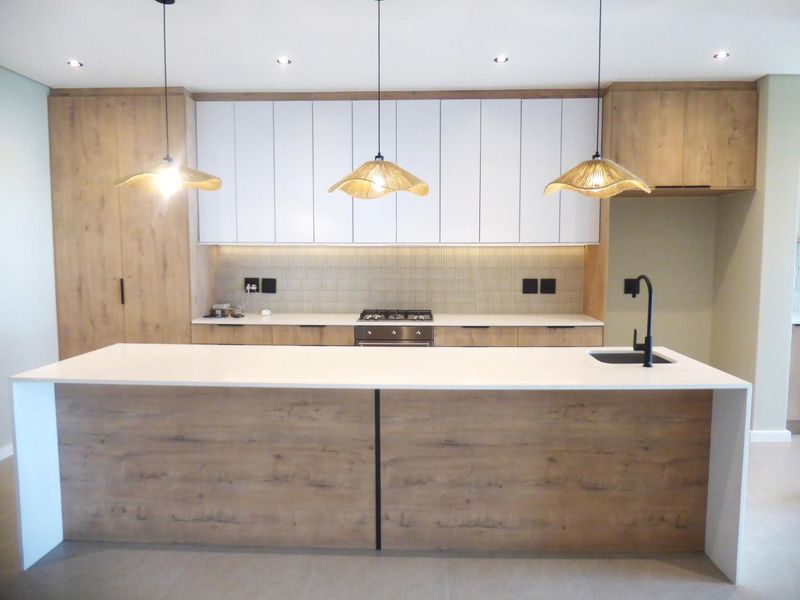 Modern kitchen featuring a large island with quartz countertops, integrated wood-grain and white cabinetry, gas hob, and contemporary lighting fixtures.