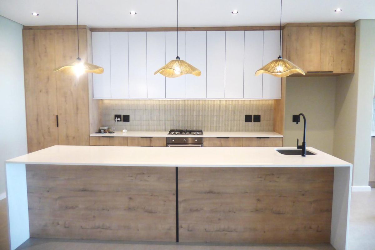 Modern kitchen featuring a large island with quartz countertops, integrated wood-grain and white cabinetry, gas hob, and contemporary lighting fixtures.