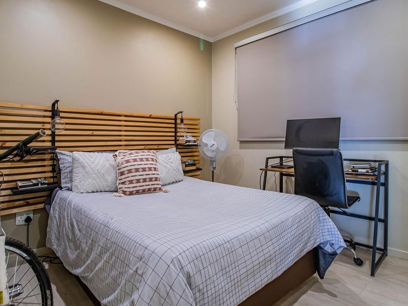 A well-maintained bedroom featuring a custom timber slat headboard, neutral wall tones, and a roller blind for privacy.