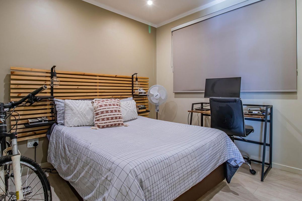 A well-maintained bedroom featuring a custom timber slat headboard, neutral wall tones, and a roller blind for privacy.