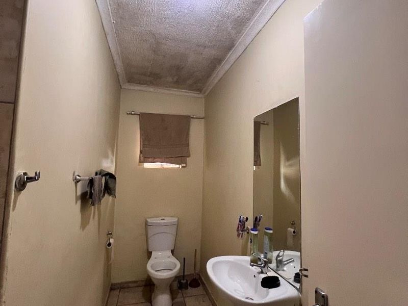 A compact bathroom featuring a pedestal basin, toilet, and tiled flooring, currently showing signs of ceiling water damage and wear.